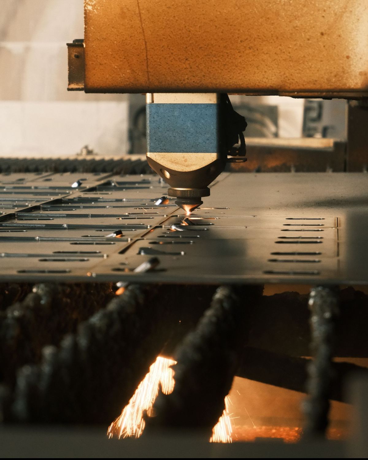 Endüstriyel lazer kesim makinesinin kesim kafası metal saca kesim yaparken; tablanın altında kıvılcımlar görülüyor